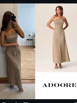 Beige axelbandslös långklänning Adoore - Superfin beige axelbandslös långklänning från Adoore med ribbad överdel och markerad V-detalj i midjan. Kjolen har vertikala ränder som ger en snygg siluett. Perfekt för dig som gillar stilrena och trendiga plagg.