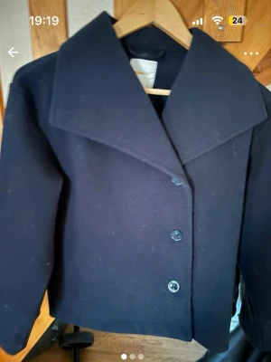 Mörkblå jacka från Gina Tricot, stl 146/152 - Klassisk mörkblå jacka med dubbelknäppning och bred krage. Jackan är gjord i ull och har en rak passform som ger en stilren look. Perfekt för dig som vill ha en tidlös och snygg jacka till höst och vinter.