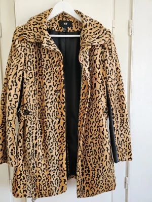 Leopardmönstrad pälsjacka från H&M - Säljer en leopardmönstrad pälsjacka från H&M med stora svarta knappar och bred krage. Jackan har bälte i midjan bara på baksidan och svarta detaljer på insidan av ärmarna. Perfekt statement-plagg för dig som vill sticka ut. Stl.38