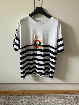 Randig t-shirt från Sinclair KappAhl strl L (42/44) - Vit och marinblå randig t-shirt från Sinclair KappAhl med broderad Royal Yachting-logga på bröstet. Klassisk passform, kortärmad och tillverkad i 100% bomull. Storlek L (42/44)