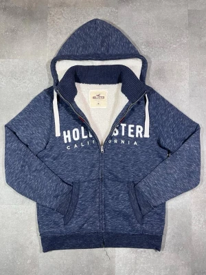 Hollister fodrad zip-up hoodie cardigan  - Säljer en Hollister fodrad zip-up hoodie cardigan i snygg marinblå färg. 🧵 Märke: Hollister 👕 Storlek: Medium 🎨 Färg: Marinblå / navy 📌 Design: Fodrad zip-up hoodie cardigan 📍 Skick: Mycket bra, se bilder!  Beskrivning: • Klassisk design från Hollister • Fodrad zip-up hoodie cardigan – varm och bekväm • Huva och dragkedja för praktisk användning • Mjuk kvalitet, perfekt för lager-på-lager • Inga fläckar, noppor eller skador (kontrollera bilder) • Lätt att matcha med jeans, chinos eller mjukisbyx