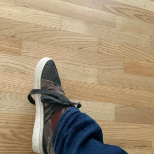 Camouflage sneakers från Steve Madden - Snygga sneakers från Steve Madden med gråsvart mesh framtill och coolt kamouflagemönster i grönt, brunt och grått på sidorna. Skorna har svarta snören och vit sula, perfekt för dig som vill sticka ut med streetstyle.