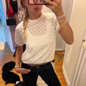 Vit stickad kortärmad topp - Säljer en vit stickad topp med korta ärmar och snyggt vågigt mönster. Perfekt för dig som gillar en fräsch och stilren look med lite twist.