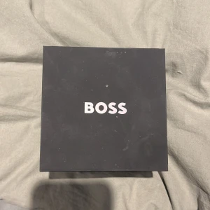 Svart och silver klocka från BOSS HELT NY aldrig använd - Stilren klocka från BOSS med svart urtavla och silverfärgat armband i metall. Klockan har guldiga visare och detaljer samt flera små urtavlor för extra funktioner. Levereras i originalförpackning med BOSS-logga.