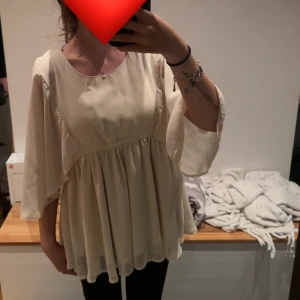 Ljusbeige flowy blus med vida ärmar - Säljer pågrund av att den är för stor storlek för mig. Jag säljer en ljusbeige blus med flowy och luftig passform. Blusen har vida, trekvartsärmar och ett rynkat midjeparti som ger en söt och avslappnad look. Tillverkad i ett tunt, lätt material som faller snyggt.
