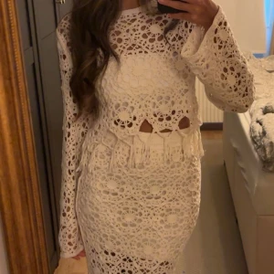 Vitt sett topp och kjol  - Superfin långklänning i vit virkad bomull med blommigt mönster och fransdetaljer vid midjan. tröjan har långärmade ärmar och en snygg omlottkänsla med öppningar vid midjan. Perfekt för sommarens alla tillfällen!, 36 men passar även 34
