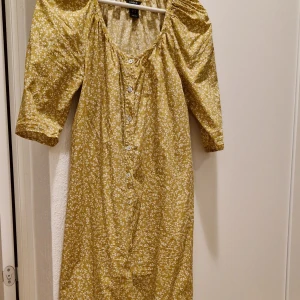Gul blommig långklänning från Lindex - Säljer en söt gul långklänning från Lindex i storlek XS. Klänningen har vitt blommigt mönster, knappar framtill och trekvartsärmar med lätt puff. Materialet är mjuk bomull och modellen har en avslappnad passform med rundad hals. Perfekt för sommarens alla tillfällen!