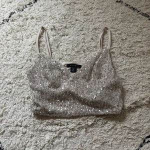 Paljettprydd silvertopp från Amisu XS - Säljer en glittrig silvrig topp från Amisu i storlek XS. Toppen har smala axelband, ärmlös design och är täckt av paljetter för en extra festlig look. Materialet är polyester med stretchig känsla. Perfekt för dig som vill sticka ut med lite extra bling.