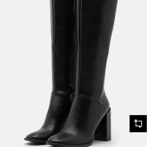 Svarta högklackade stövlar RAID - Snygga svarta högklackade stövlar från RAID i slätt skinnliknande material. Modellen har spetsig tå, blockklack och dragkedja på insidan för enkel påtagning. Perfekt för dig som vill ha en stilren och trendig look med extra höjd.