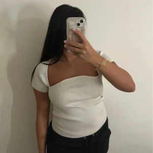Vit ribbad offshoulder topp - Säljer en snygg vit ribbad topp med offshoulder-design och kort ärm. Toppen har en asymmetrisk halsringning som ger en modern vibe och är tillverkad i ett stretchigt material som sitter tight. Perfekt att styla med jeans eller kjol.
