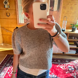 Grå stickad kortärmad tröja - Supermysig grå stickad tröja med korta puffärmar och rund hals. Modellen är lite croppad och har en loose fit som ger en chill vibe. Perfekt att styla med jeans eller kjol för en enkel men snygg look.