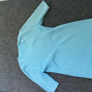 Blå ribbad T-shirt Storlek S/XS - Säljer en ljusblå ribbad tshirt med trekvartsärm och rund hals. T-shirten har ett coolt geometriskt mönster framtill som ger extra edge. Perfekt för dig som gillar stilrena men ändå unika plagg.