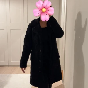 Svart teddyjacka med knappar - Mysig svart teddyjacka med stora slag och knäppning framtill. Jackan har lång ärm och är tillverkad i ett fluffigt teddy-material som ger en cool och avslappnad vibe. Perfekt för kyliga dagar när du vill vara både varm och snygg. Använd endast ett fåtal gånger