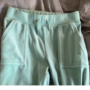 Mintgröna mjukisbyxor Juicy Couture - Supermjuka mintgröna mjukisbyxor från Juicy Couture med bred resår i midjan, snörning och stora fickor fram. Bakficka med lock och tryckknappar. Perfekta för chill eller streetwear-vibe. Använda ett fåtal gånger ❤️