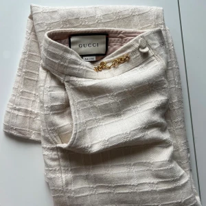 Gucci vita kostymbyxor med kedjedetalj - Vita vintage kostymbyxor från Gucci med rutigt strukturmönster och snygg guldfärgad kedjedetalj i midjan. Byxorna har rak passform, hög midja. Lite stora för mig men passar min mamma som har storlek S/M! 