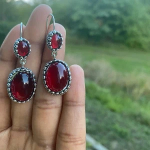 Röda statement örhängen i silverfärg - Säljer ett par snygga örhängen med stora, ovala röda stenar infattade i silverfärgad metall. Örhängena har en vintagekänsla med detaljer runt stenarna och hängande design. Perfekta för att lyfta vilken outfit som helst.