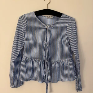 Blå och vitrandiga skjorta/blus  - Blå och vitrandiga skjorta/blus i str S från Stradivarius. Tre knyten framtill och volangdetalj. Material som en skjorta fast mjukare och lättare 