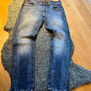 Blå jeans från Jack & Jones - Snygga blå jeans från Jack & Jones med klassisk femficksdesign. Jeansen har orangea detaljer och broderade bakfickor. De är raka i modellen och har en normal passform. Perfekta till sneakers och hoodie.