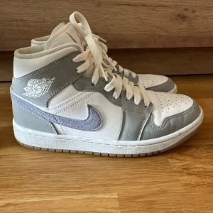 Nike Air Jordan 1 Mid vit/grå 38.5 - Säljer mina fina Nike då de inte passar mig. Använda vid enstaka tillfällen ca 3ggr så de är i princip i nyskick. Färgen heter Wolf grey. Nypris ligger på 2200kr