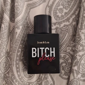 Jean & Len Bitch Please Eau de Toilette - Parfymflaska i svart glas med texten 'Bitch Please' i vitt och rött samt guldfärgad logga. Flaskan är fyrkantig med rund svart kork och rymmer 30 ml Eau de Toilette. Modern och edgy design, perfekt för dig som gillar att sticka ut.