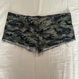 Camouflage shorts med fransig kant - Säljer ett par coola camouflage-mönstrade shorts med låg midja och fransig kant. Färgerna är grönt, svart och grått, och materialet är klassisk jeans. Shortsen har fickor både fram och bak samt hällor för bälte. Perfekt för dig som gillar streetstyle.