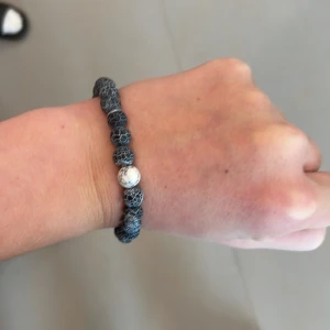 Svart pärlarmband med mönster - Snyggt svart armband med pärlor som har ett coolt nätmönster och en vit marmorerad pärla som detalj. Perfekt för dig som vill ha något unikt på handleden. Passar både killar och tjejer och är lätt att matcha med andra accessoarer.