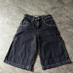 Jorts - Säljer ett par svarta jeansshorts från Bershka i loose fit. De har klassisk femficksdesign, knapp och dragkedja framtill samt breda ben som slutar strax under knät. Perfekta för en chill och avslappnad stil.