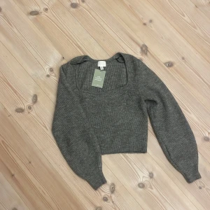 Grå croppad stickad tröja H&M - Säljer en grå croppad stickad tröja från H&M med långärmade puffärmar och fyrkantig halsringning. Tröjan är ribbad. Aldrig använd 