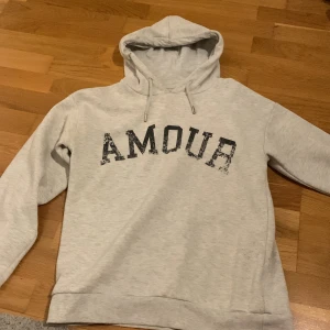 Ljusgrå hoodie med tryck - Ljusgrå hoodie från Gina Tricot med svart texten 'AMOUR' framtill och en stjärna på ryggen. Har växt ut den, men den är knappt använd 💕