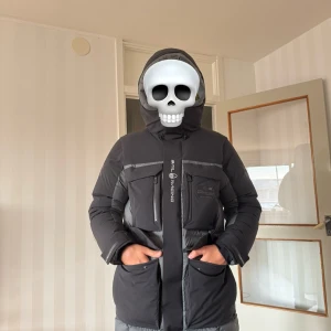 Sail Racing dunjacka Gore-Tex svart/grå - Säljer en Sail Racing Antarctica dunjacka med Gore-Tex. Jackan är svart och grå med gul insida, har huva, flera fickor med dragkedja och Sail Racing-logga på bröstet. Storlek M