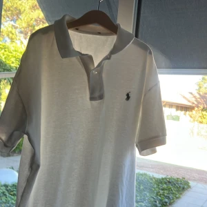 Vit pikétröja från Ralph Lauren - Klassisk vit pikétröja från Ralph Lauren med korta ärmar och broderad logga på bröstet. Tröjan har krage och knäppning framtill. Perfekt för en clean och stilren look.