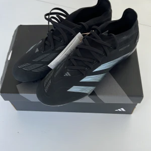 Adidas Predator Pro FG fotbollsskor - Adidas Predator Pro FG i svart med silvriga detaljer. Skorna har snörning och är designade för fotboll på naturgräs. Snygg, modern look. Aldrig testade med kvitto