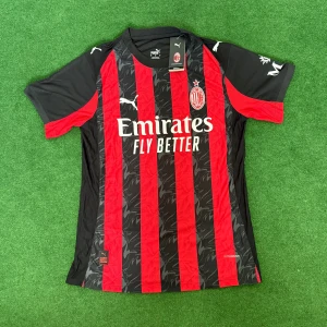 AC Milan Puma matchtröja 25/26 - AC Milan matchtröja från Puma med klassiska röda och svarta ränder, klubbmärke på bröstet och sponsortryck framtill. Tillverkad i lätt och ventilerande polyester, kortärmad modell med svarta och röda detaljer på ärmarna. Perfekt för fotbollsälskare!