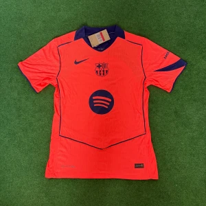 Barcelona Nike orange matchtröja 25/26  - Säljer en officiell FC Barcelona matchtröja från Nike i orange med mörkblå detaljer. Tröjan har klubbmärke, Nike-logga och Spotify som sponsor framtill samt UNHCR-tryck bak. Tillverkad i lätt och ventilerande funktionsmaterial, perfekt för fotbollsträning.
