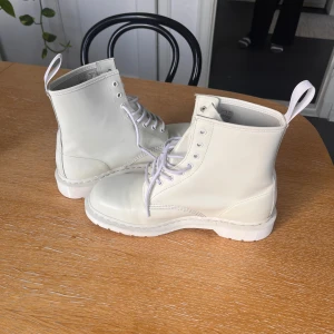 Vita Dr. Martens boots i skinn - Säljer ett par vita Dr. Martens boots i storlek 45. Skorna är i skinn med klassisk snörning, rund tå och grov sula. Perfekta för dig som vill sticka ut med ett par stilrena och tidlösa boots. Passar till både jeans och kjol för en edgy look.