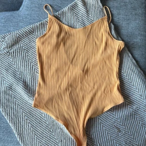 Ribbad body orange från H&M - Snygg ribbad body  från H&M i en fräsch orange färg. Modellen har smala axelband och en rundad rygg, Materialet är mjukt och stretchigt syntet som sitter skönt mot kroppen. Passar dig som vill ha en enkel men trendig look i sommar.