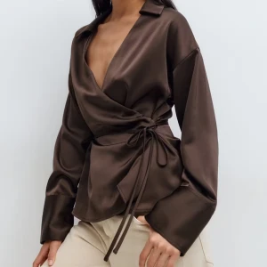 Brun omlottblus med snörning - Snygg brun omlottblus i satin med v-ringad design och långa ärmar. Har kvar prislappen, i nytt skick! 