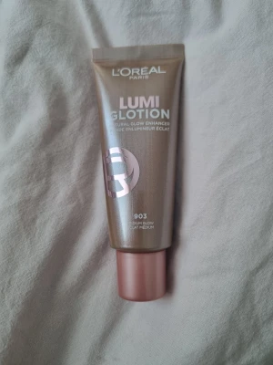 L'Oréal Lumi Glotion 903 Medium Glow - Glow enhancer från L'Oréal Paris i nyansen 903 Medium Glow. Tuben rymmer 40 ml och har en skimrande brun färg med roséguldigt tryck och rosa kork. Flytande formula som ger huden en naturlig lyster och kan användas som highlighter eller under foundation. Helt ny