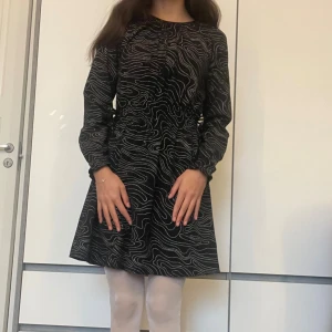 Svart glittrig klänning från H&M - Svart klänning från H&M med glittrigt silvermönster och snygga snörningsdetaljer i midjan. Klänningen har långärmade ärmar och rund hals, perfekt för nyårsfest. Materialet är mjukt och bekvämt. Har använt den endast 2 gånger. (Var snäll och lajka om du är intresserad av klänningen så att jag vet)💕