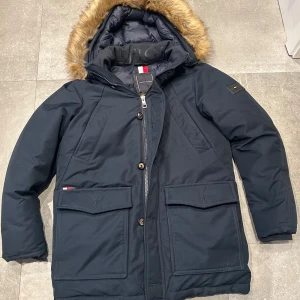 Tommy hilfiger parks jacka  - En varm och snygg parka till vintern, denna jacka har fyra fickor på framsidan och en avtagbar luva samt pälss till som också går att ta av och på, jackan är i näst till oanvänt skick och i storlek M