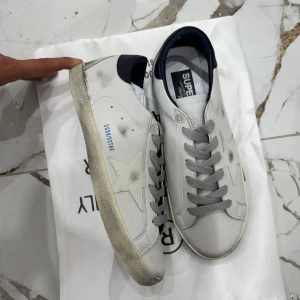 Golden Goose vita sneakers med stjärna - Säljer ett par snygga Golden Goose sneakers i vitt skinn med grå snörning och en ikonisk stjärndetalj på sidan. Helt oanvända dem är äkta 