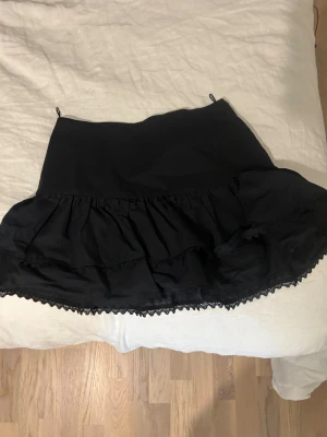 Svart volangkjol från Zara XS - Supersöt svart kortkjol från Zara med dubbla volanger och spetskant längst ner. Kjolen har en hög midja och är gjord i ett mjukt bomullsmaterial. Perfekt för dig som gillar en feminin och trendig look.