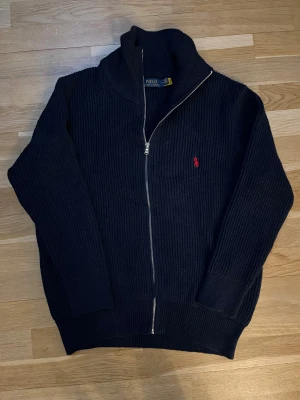 Marin blå stickad kofta från Polo Ralph Lauren - Det Helt ny och superpopular troja! Aldrig använts, i nyskick. Trojan ar tjock, varm och perfekt for vintern, bäde for en fin och bekvam look. Trojan ar unisex och passar bra for bäde kvinnor och man. Säljer den pä grund av storleken. Den är i storlek M. Passar dig som är ungefär 170-190 cm lăng och vager 65-85kg. För dig som söker julklapp är denna tröja perfekt! & Hör gärna av dig om du har nagra fragor eller funderingar!