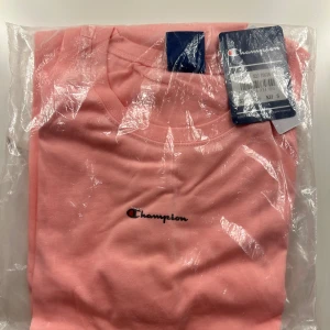Rosa Champion t-shirt i bomull - Fräsch rosa t-shirt från Champion som aldrig använts. Modellen är kortärmad och har en rund halsringning. Tillverkad i mjuk bomull som känns skön mot huden. 