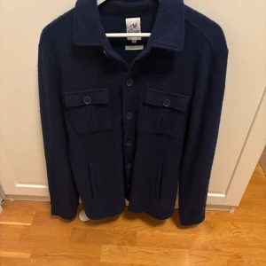 Marinblå overshirt i 100% ull - Schysst marinblå overshirt från John Partridge i 100% ull. Perfekt nu uinför kallare väder men även för lager på lager. Pris är förhandlingsbart, de e ba ba skriva vid frågor och funderingar