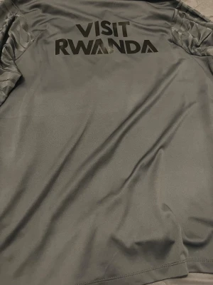 PSG långärmad träningsöverdel Nike - Snygg grå långärmad PSG-fotbollströja från Nike med halv dragkedja, svarta och röda detaljer samt diskret mönster på ärmarna. Tillverkad i lätt och ventilerande funktionsmaterial, perfekt för träning eller match.