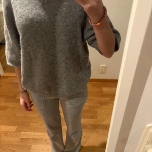 Grå stickad tröja & Other Stories - Mysig grå stickad tröja från & Other Stories med rund hals och trekvartsärm. Tröjan har en loose passform och är tillverkad i mjukt material som passar perfekt för kyliga dagar. Enkel och stilren design som är lätt att matcha med allt.