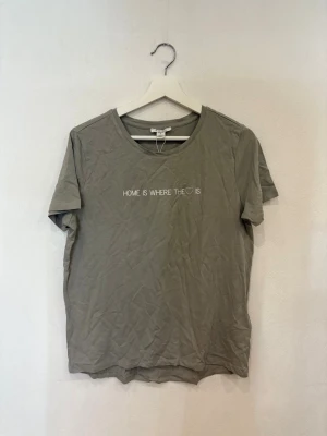 Grå t-shirt från Amisu med tryck - Snygg grå t-shirt från Amisu med rund hals och korta ärmar. Framsidan har ett stilrent tryck med texten 'HOME IS WHERE THE ♥ IS' i vitt. Mjuk och skön bomullskvalitet, perfekt för en chill look. Enkel design som funkar till jeans eller shorts.