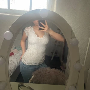 Vit spetsblus Gina - Säljer en vit blus i spets med v-ringad hals och korta ärmar. Toppen har figurnära passform och fina spetsdetaljer över hela plagget. Perfekt för dig som gillar romantisk och feminin stil.