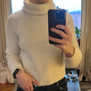 Vit polotröja från Chiquelle - Säljer en vit polotröja från Chiquelle med grovstickad struktur och hög krage. Tröjan har långärmade raglanärmar och är gjord i ett mjukt stickat material som känns riktigt cozy. Perfekt för kyliga dagar och enkel att styla med jeans eller kjol.